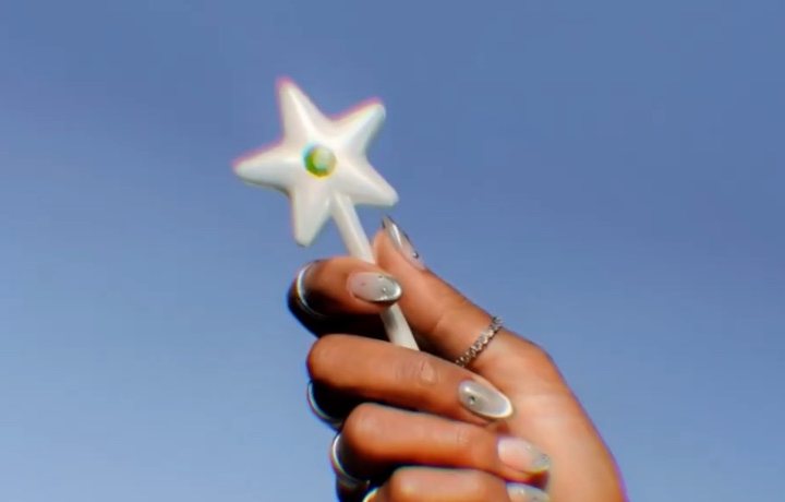 A hand holds the pearl Wand up against a blue sky