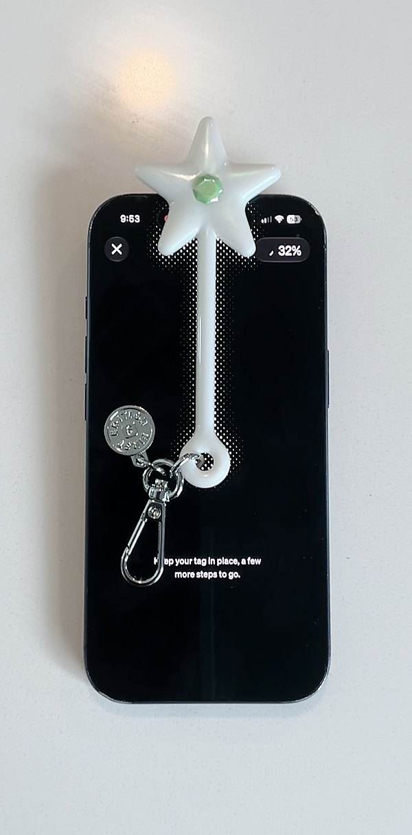 In hand: the Wand lies on top of the phone, its star hanging off the top edge, while the screen says Keep your tag in place, a few more steps to go. The tag is about as long as the phone